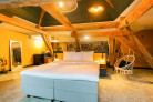Overzicht van de Deluxe Suite met karakteristieke houten balken een tweepersoons King Size bed, schommelstoel en spiegel