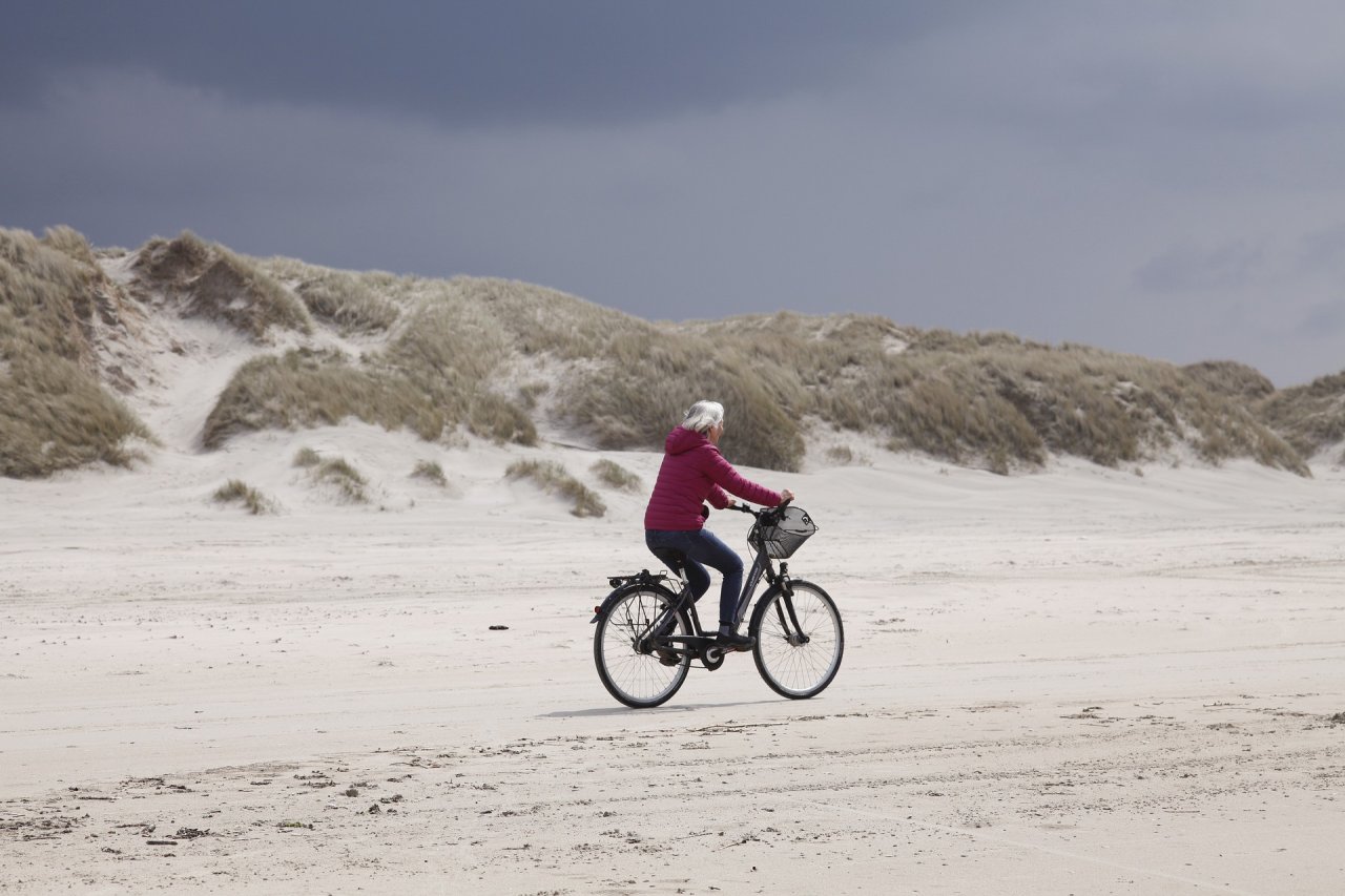 Vrouw-op-de-fiets-op-het-strand-lekker-uitwaaien.